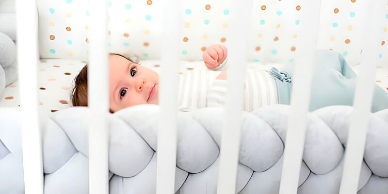 Bébé dans un berceau entouré par une tresse de lit grise